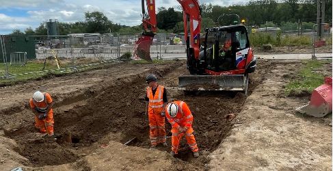 Workers in high viz digging along with a digger on a construction site.