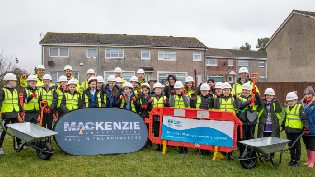 A group of children in hi vis stand in front of signage outdoors, preparing to plant a tree