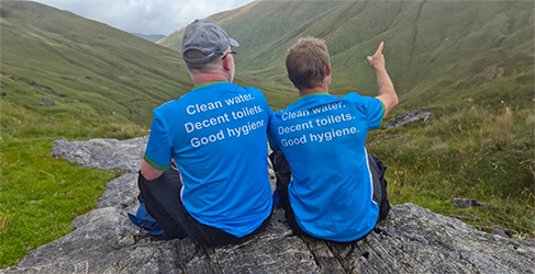 Two climbers from the back looking up at CisteDhubh munro wearing WaterAid Tshirts with Clean Water, Decent toilets, Good hygiene printed on the back